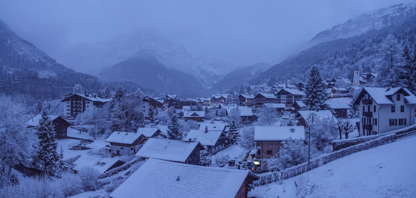 Village de montagne enneigé au crépuscule, au fond d'une vallée