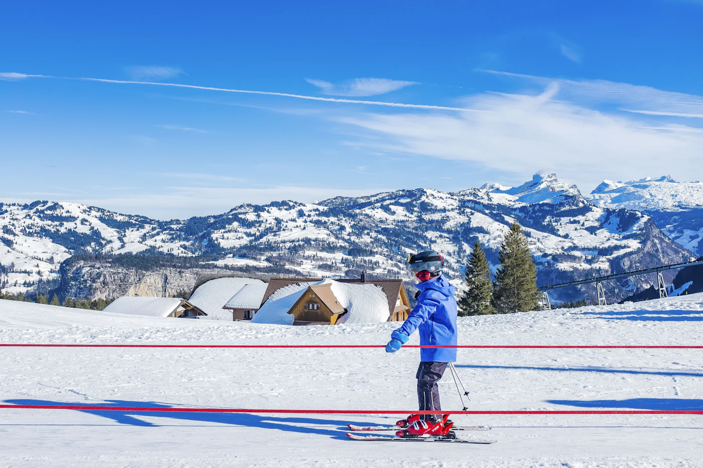Enfant qui skie sur une piste ensoleillée, sommets enneigés en arrière-plan